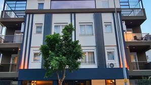 A modern hotel with a prominent sign, multiple balconies, and a tree in front. - Sun Suite (Antalya)