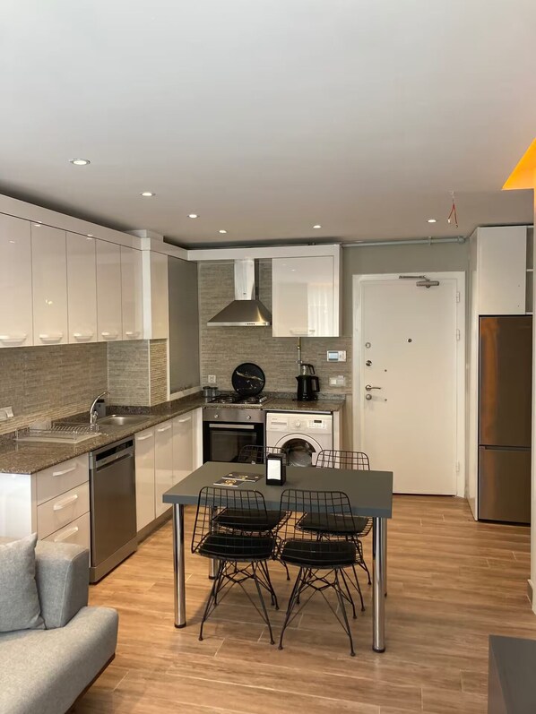 A modern kitchen with a dining area, built-in appliances, and a grey sofa. - Sun Suite (Antalya)