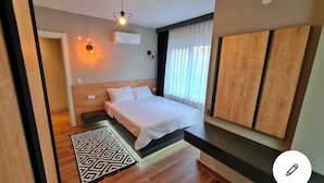 A modern bedroom with a wooden headboard, a bed with white bedding, a geometric-patterned rug, and a wall-mounted air conditioner. - Sun Suite (Antalya)