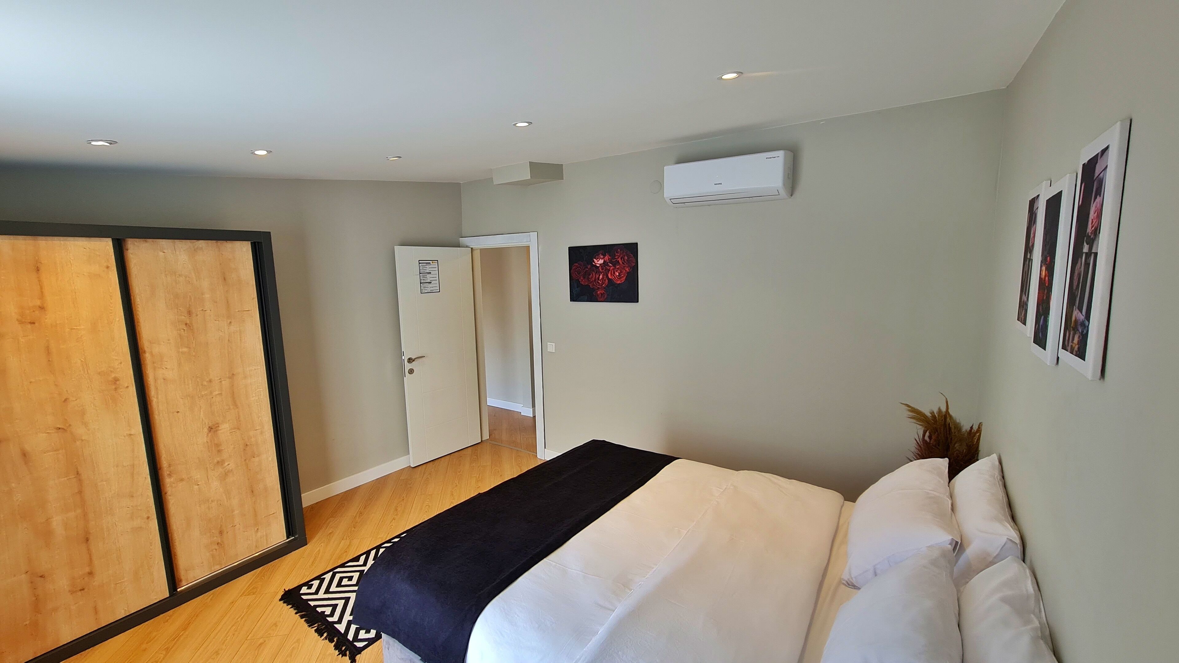 A bedroom with a bed, a wardrobe, a door, an air conditioner, and a wall-mounted picture frame.