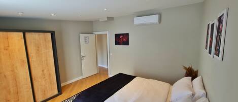 A bedroom with a bed, a wardrobe, a door, an air conditioner, and a wall-mounted picture frame.