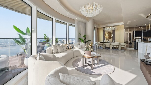 Un salon moderne avec un grand canapé d’angle, une table basse ronde et un lustre. On y trouve également un coin repas agrémenté d’un lustre et offrant une vue sur la ville.