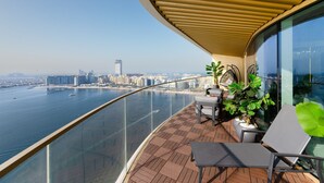 Un balcon avec vue sur les toits d’une ville et sur l’eau. On y trouve deux chaises et une plante en pot.