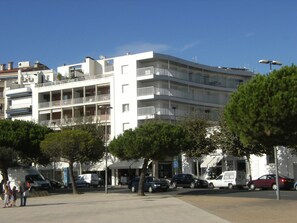 A multi-story building with balconies, a parking area, and trees.