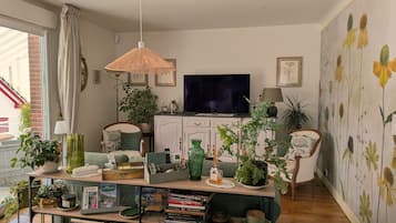 Un salon avec une télévision, des livres, des plantes et un mur décoratif.