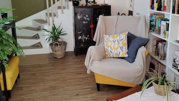 Un salon avec un fauteuil jaune, un plancher en bois, une bibliothèque, un escalier et une plante en pot.