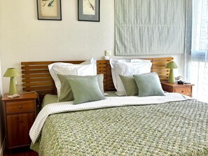 Une chambre à coucher bien rangée, avec une tête de lit en bois, une couette verte et une table de chevet sur laquelle se trouve une lampe.