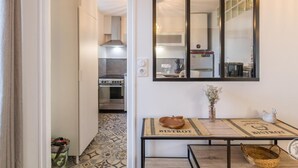 Una cocina compacta con estufa, horno y electrodomésticos modernos. Se observa un comedor con una mesa y sillas, con un mantel individual que muestra la palabra "BISTROT".