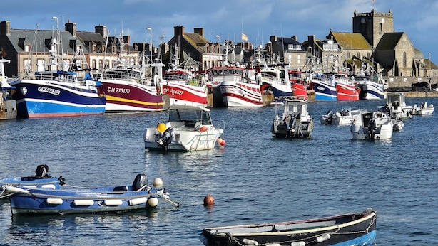 Un puerto con varios barcos amarrados, una imponente torre de iglesia y una hilera de edificios a lo largo del paseo marítimo.