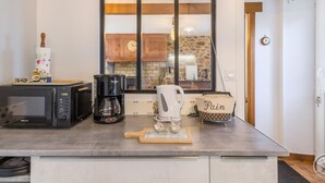 Una cocina con microondas, cafetera, hervidor y rodillo sobre la encimera.