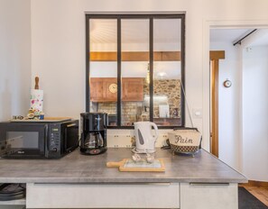 Uma cozinha com micro-ondas, cafeteira, chaleira e um rolo de massa em cima do balcão.