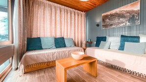 Una habitación acogedora con techo de madera, un ventanal con cortinas, una mesa de madera y dos camas con ropa de cama estampada.