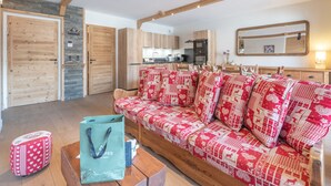 Una sala de estar acogedora con un sofá estampado, vigas de madera, una pared de piedra y una cocina al fondo.