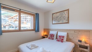 Un dormitorio con cabecera de madera, una cama grande con ropa de cama blanca, dos mesitas de noche con lámparas, una ventana con vistas a edificios y un cuadro enmarcado en la pared.