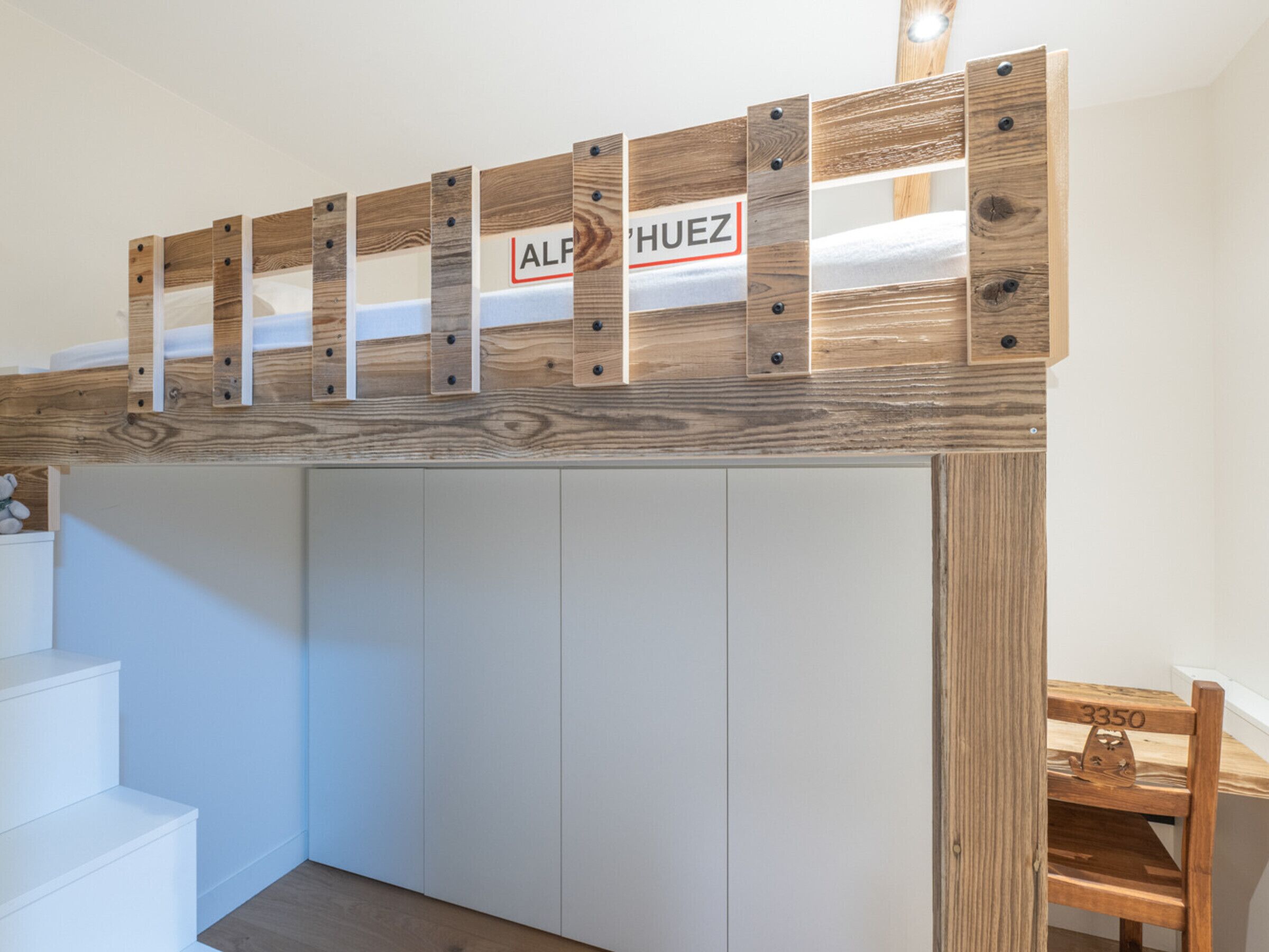 A room with a wooden shelf above a white wardrobe, a wooden chair with a number, and a staircase.