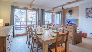 Un comedor con una mesa de madera dispuesta para seis personas, ventanas amplias y vistas a una estación de esquí.