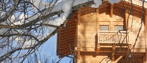 Eine Holzhütte mit Balkon, umgeben von schneebedeckten Ästen und Bäumen.