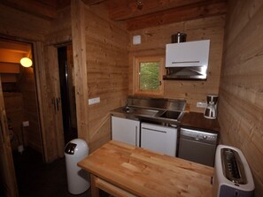Una cocina compacta con paredes de madera, una ventana, un lavabo, una estufa y una mesa pequeña.