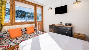A bedroom with a bed, a dresser, a television, and a window with a view of a snowy landscape. - Renovated Studio Cabin - On the Slopes at Plagne Centre (La Plagne-Tarentaise)