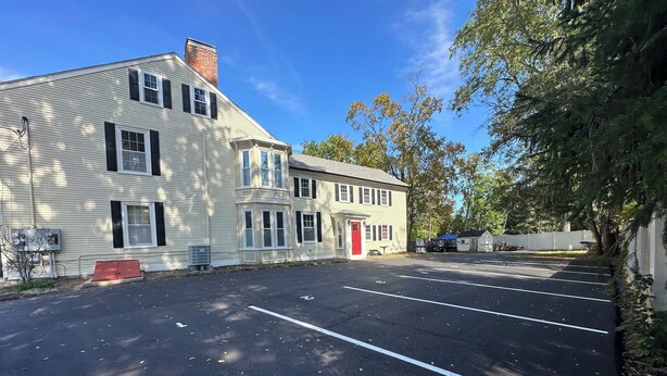A parking lot with a building that has a red door and multiple windows. - Liz Room in downtown Exeter next to PEA (Exeter)