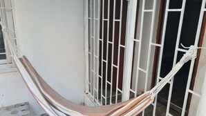 A hammock tied between a white wall and a metal gate, with a wooden floor visible below.