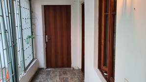 A hallway with a wooden door, a window with a wooden frame, and a wall-mounted light fixture.