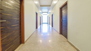 A long, well-lit hallway with polished floors, wooden doors, and a skylight at the end. - Hotel Shivansh (Jaipur)
