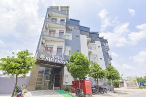Un hotel de varios pisos con diseño moderno, que cuenta con balcones, unidades de aire acondicionado y una rampa de acceso verde.