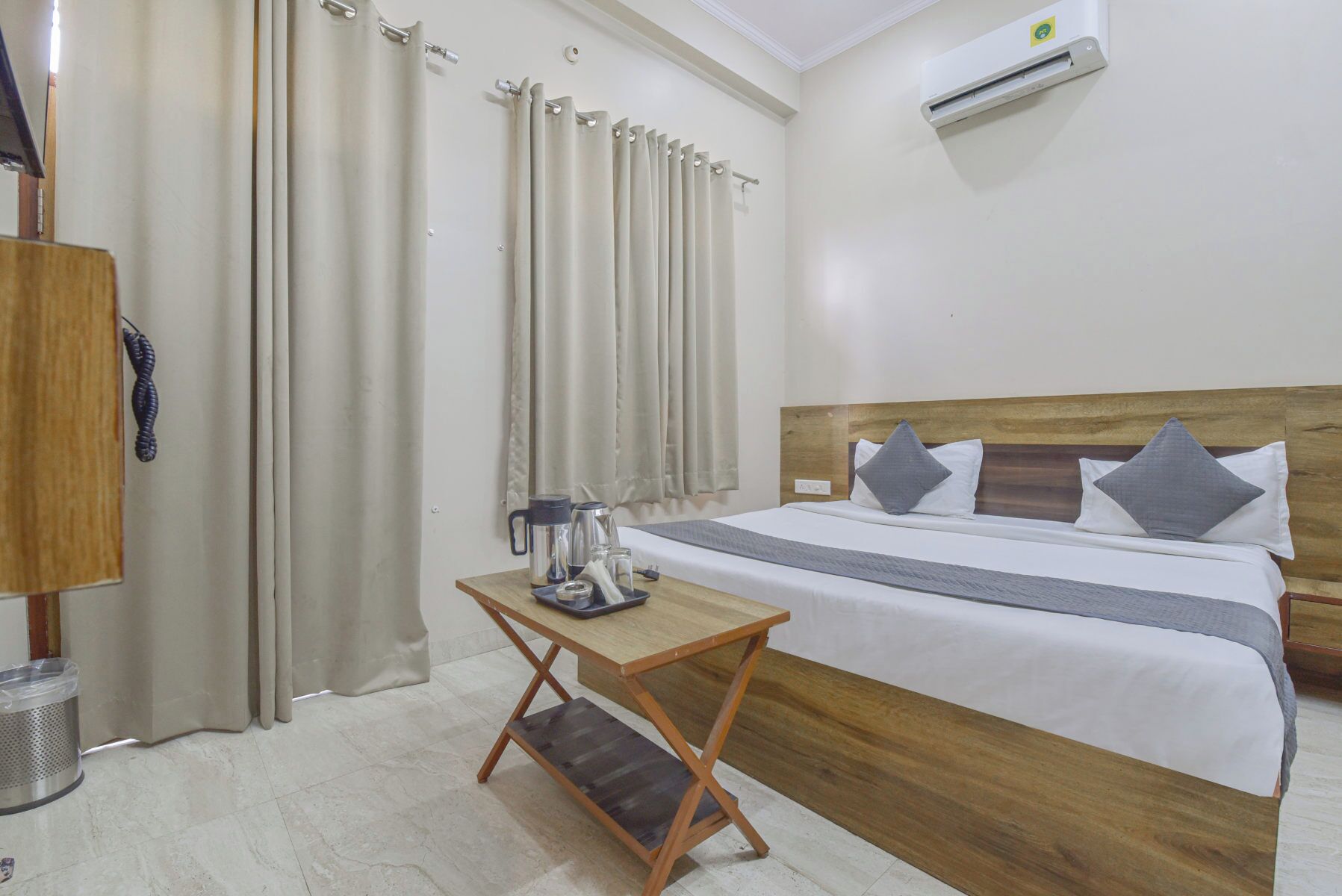 A hotel room with a bed, a small wooden table, a coffee maker, and a trash bin.