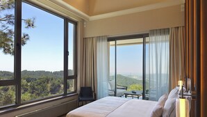 A bedroom with a large bed, a chair, a table, and a view of the outdoors.