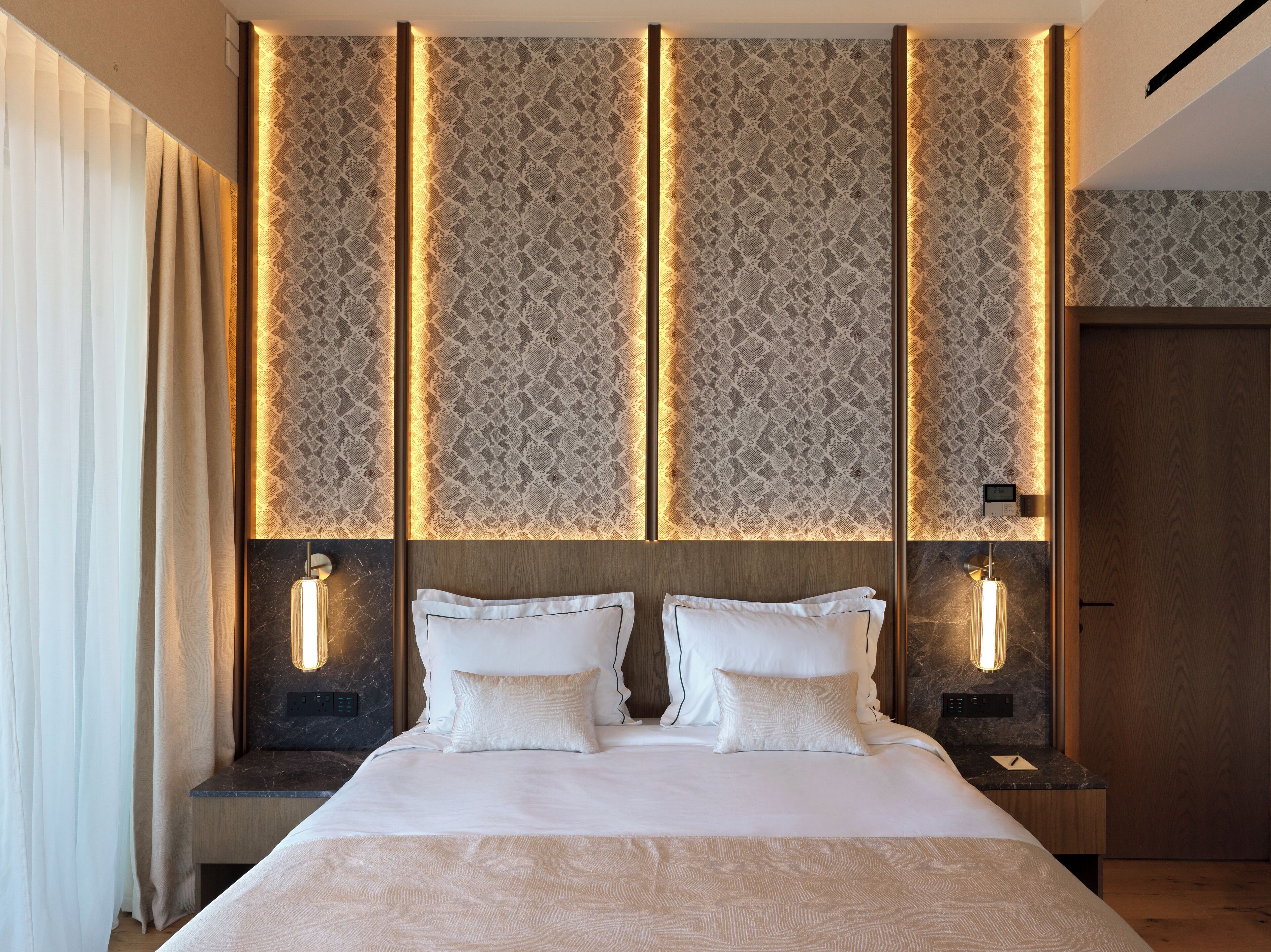 A modern hotel room with a large bed, two bedside tables, and a wall with vertical light panels.