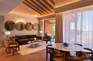 Una sala de estar moderna con sofá, sillones, una mesa de centro y una mesa de comedor. Hay ventanas grandes con cortinas, un techo con vigas de madera y espejos colocados en las paredes.