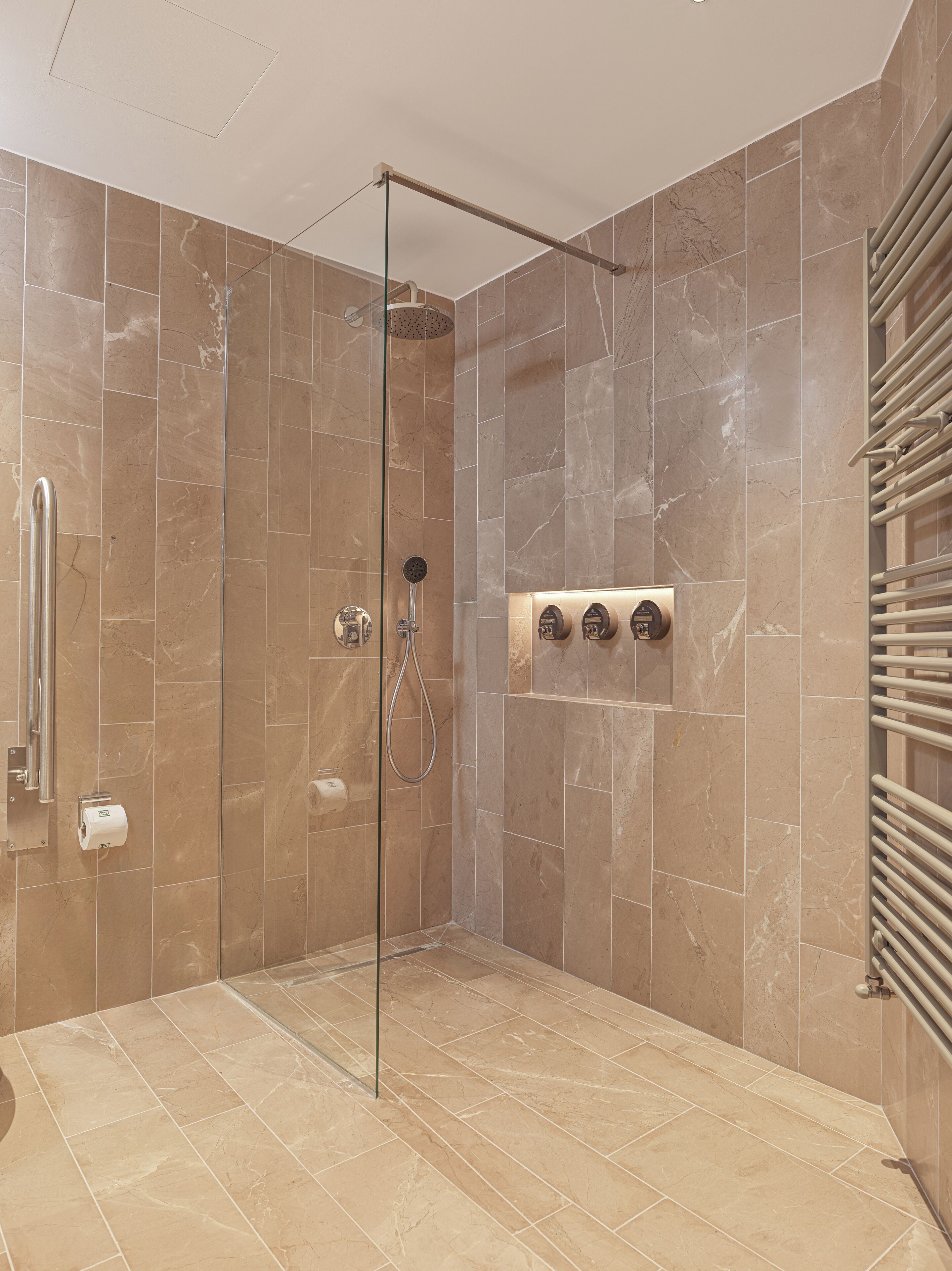 A walk-in shower with a glass door, marble tiles, a towel rack, and a hand dryer.
