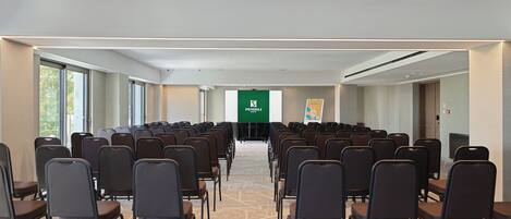 A conference room with rows of chairs facing a presentation screen, a carpeted floor, and a door on the right.