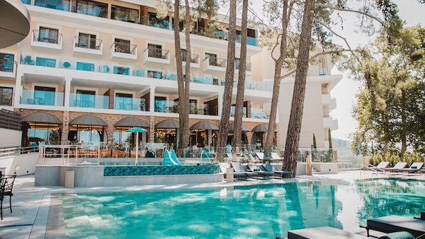 A hotel with a swimming pool, lounge chairs, and a slide.