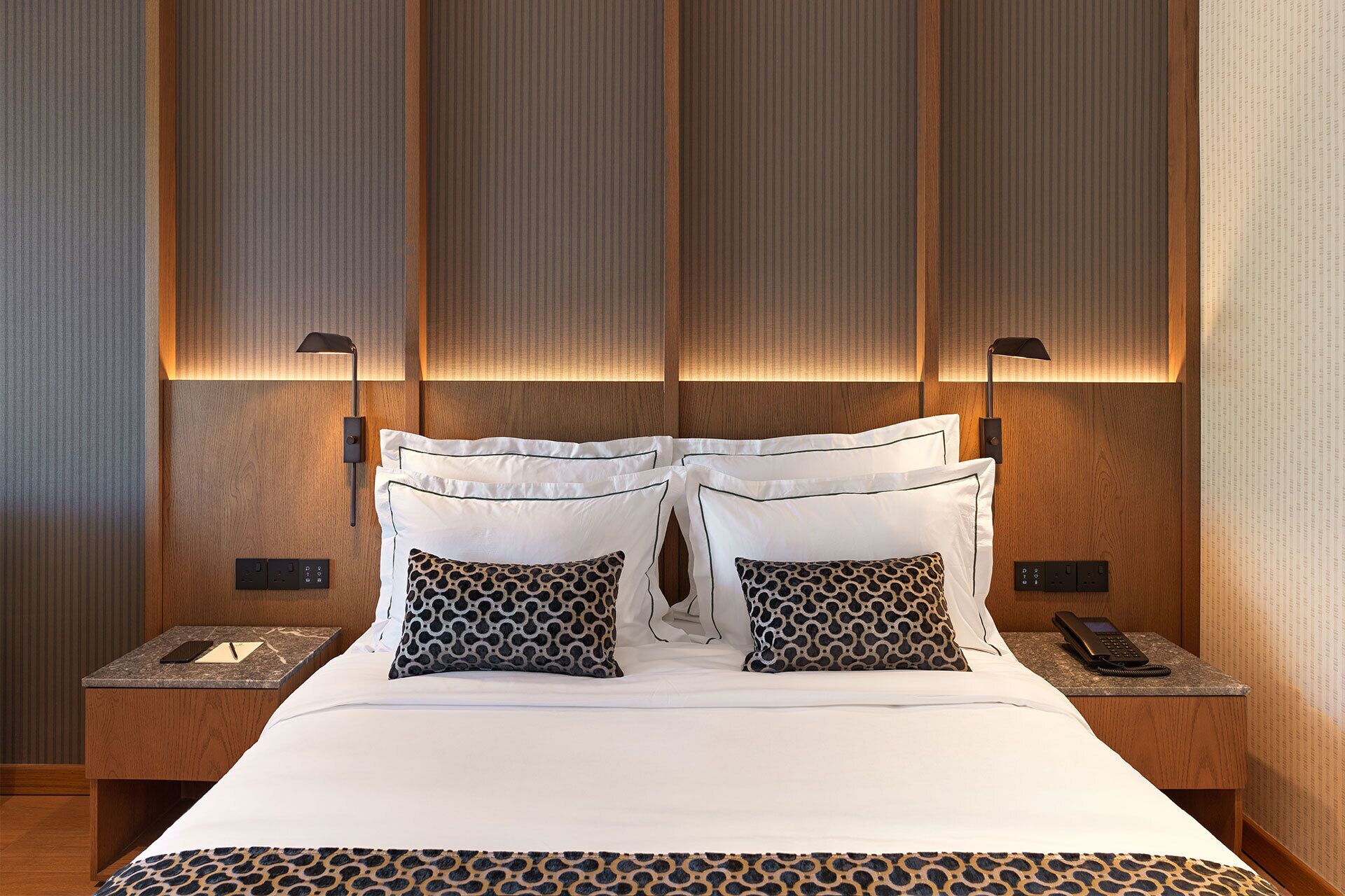 A hotel room with a large bed, two bedside tables, a telephone, and a wall-mounted lamp.