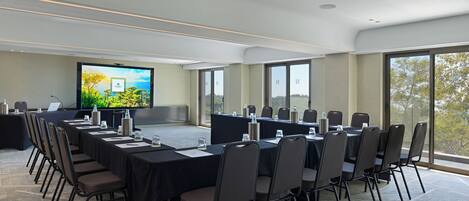 Una sala de conferencias con una pantalla grande, varias mesas y sillas dispuestas para reuniones.