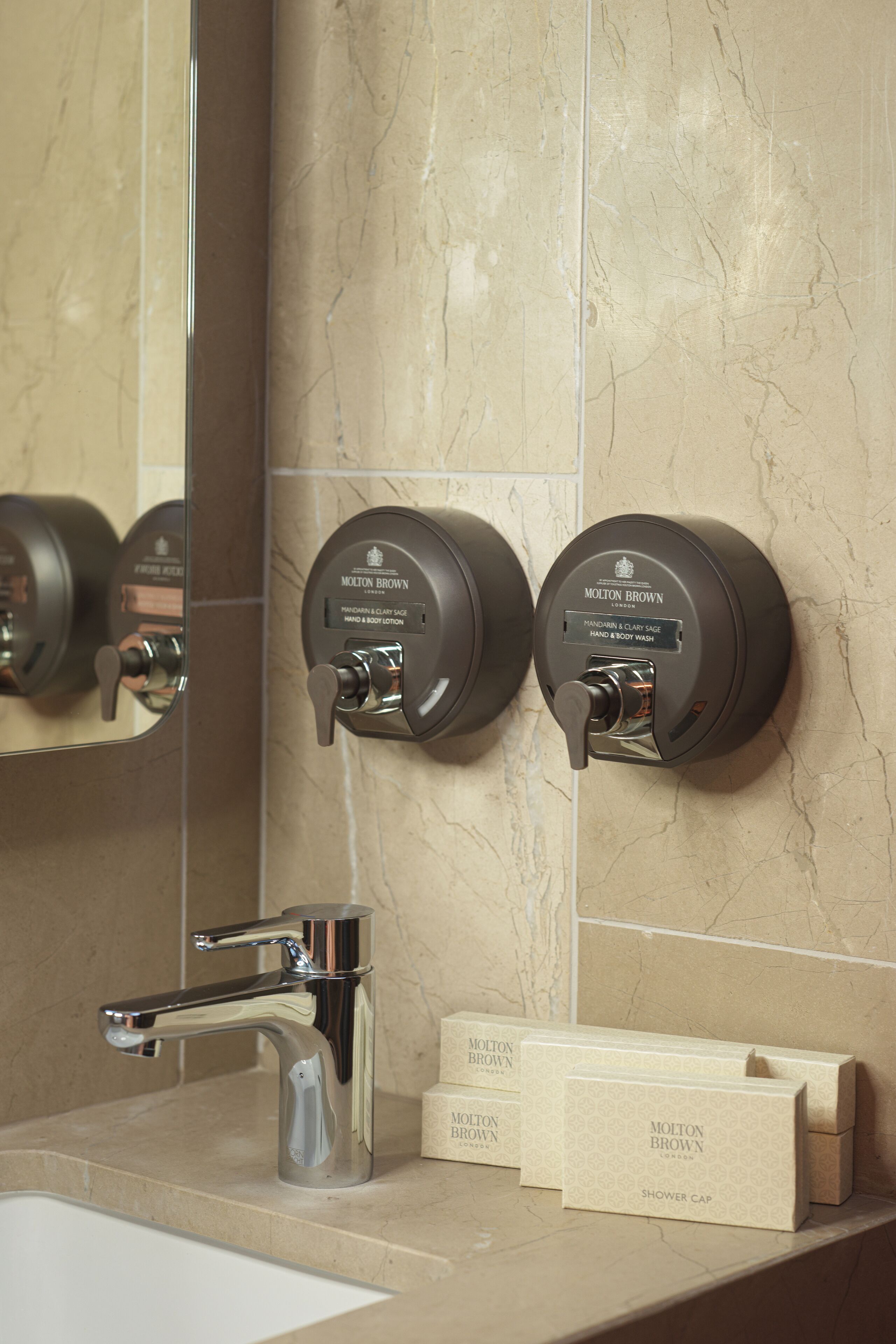 A bathroom with a marble wall, a chrome faucet, and two hand and body wash dispensers labeled 'Molton Brown'.