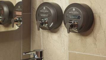 A bathroom with a marble wall, a chrome faucet, and two hand and body wash dispensers labeled 'Molton Brown'.