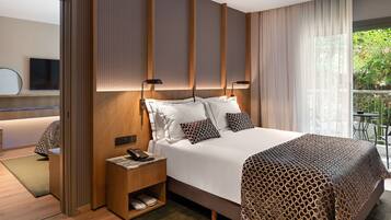 A modern hotel room with a large bed, a bedside table with a phone, and a view of greenery outside.