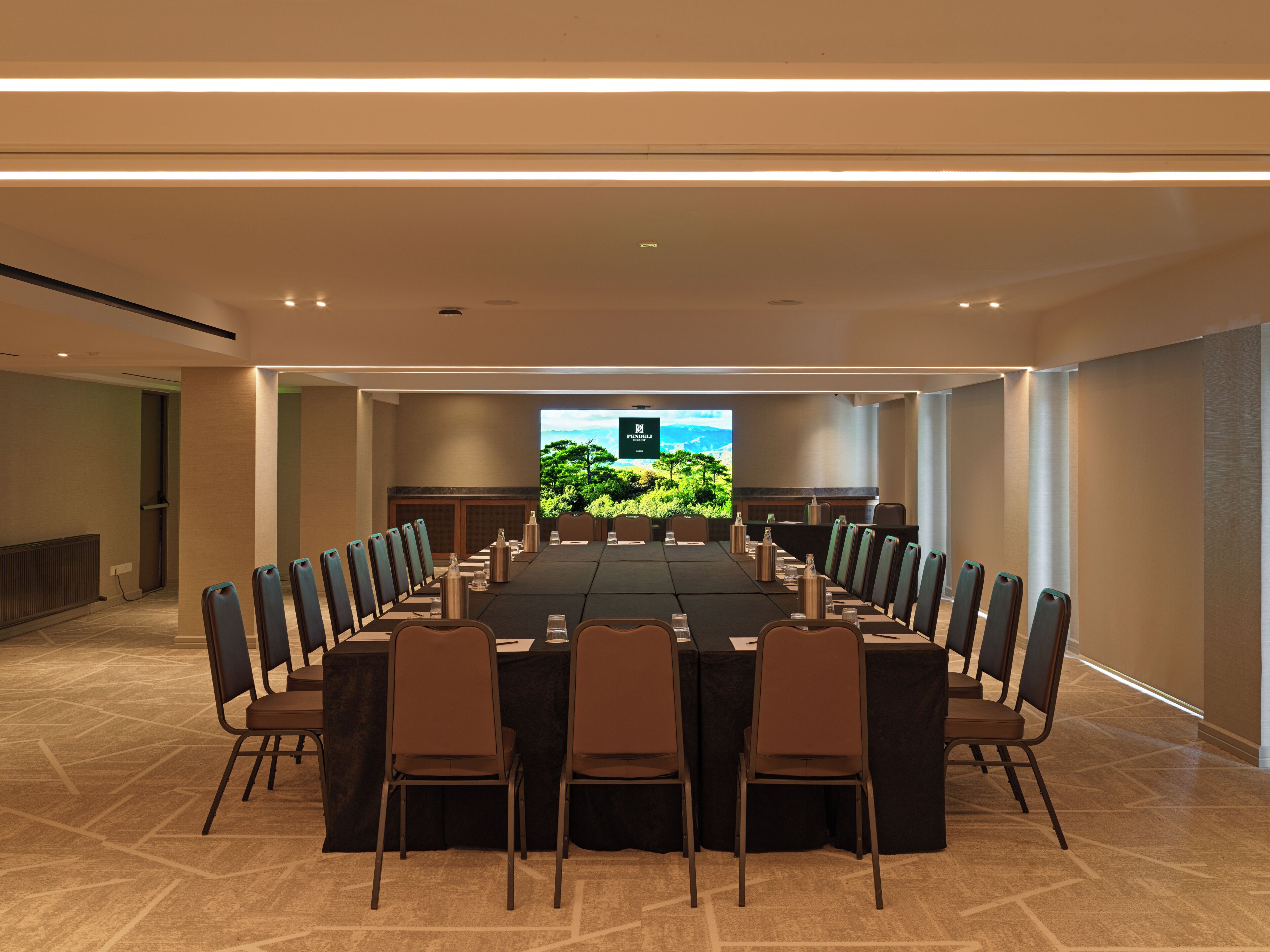A conference room with a long table, chairs, and a large screen displaying a scenic view.
