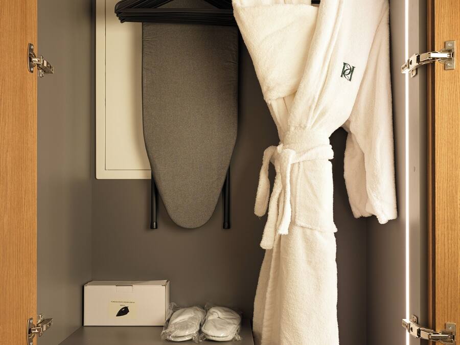 Habitación de hotel con bata colgada en un perchero, un toallero y un minibar con control remoto.