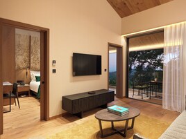 Una habitación de hotel moderna con televisor de pantalla plana en la pared, un armario de madera, una mesa de centro redonda con un libro y un balcón con vistas a árboles.