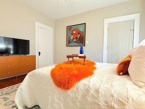 Un dormitorio con una cama, televisor, un cuadro y una puerta.