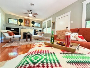 A living room with a fireplace, a sofa, a coffee table with snacks, and a ceiling fan. - Stylish Abilene Home - Berry Suites (Abilene)