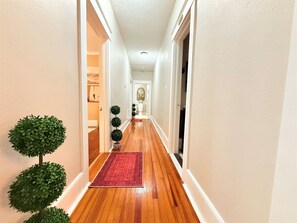 Un couloir doté d’un plancher en bois, d’un tapis rouge et de plantes ornementales vertes taillées en forme.
