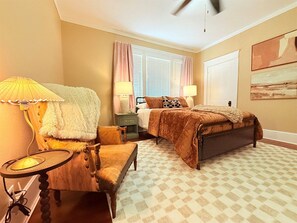 A bedroom with a bed, two bedside tables, a chair, a lamp, a window with curtains, and a ceiling fan. - Stylish Abilene Home - Berry Suites (Abilene)
