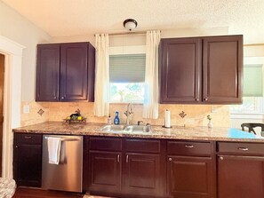 A kitchen with dark cabinets, a stainless steel refrigerator, a double sink, and a window with curtains.