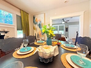 Una mesa de comedor dispuesta con posavasos, platos y vasos, con un florero de flores en el centro.