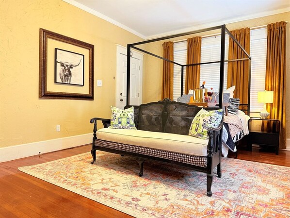 Una cama con dosel y cortinas, un sofá con cojines estampados, un cuadro enmarcado en la pared y una alfombra con diseño en el suelo.